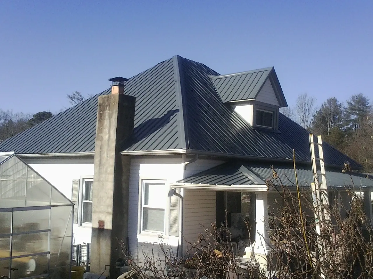Dark blue standing seam metal roof on a white farmhouse with dormer — Slate & Tile Roof Repair by Roofing Brothers in Cheswick