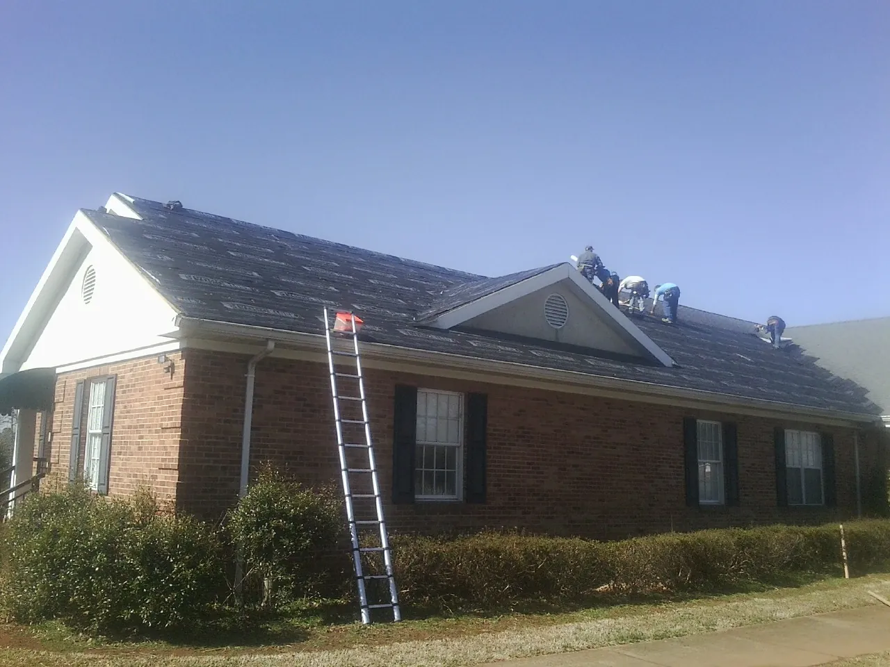 Crew tearing shingles off a brick ranch roof with a ladder set — Emergency Roof Repair work by our crew in Cheswick