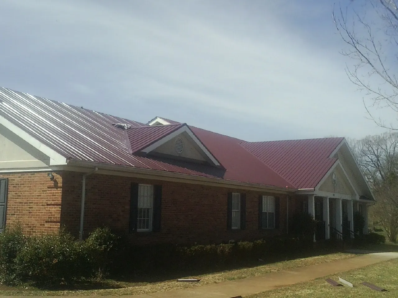 Red metal roof with gabled entries on a long brick building, from a Hail Damage Roof Repair job in Cheswick