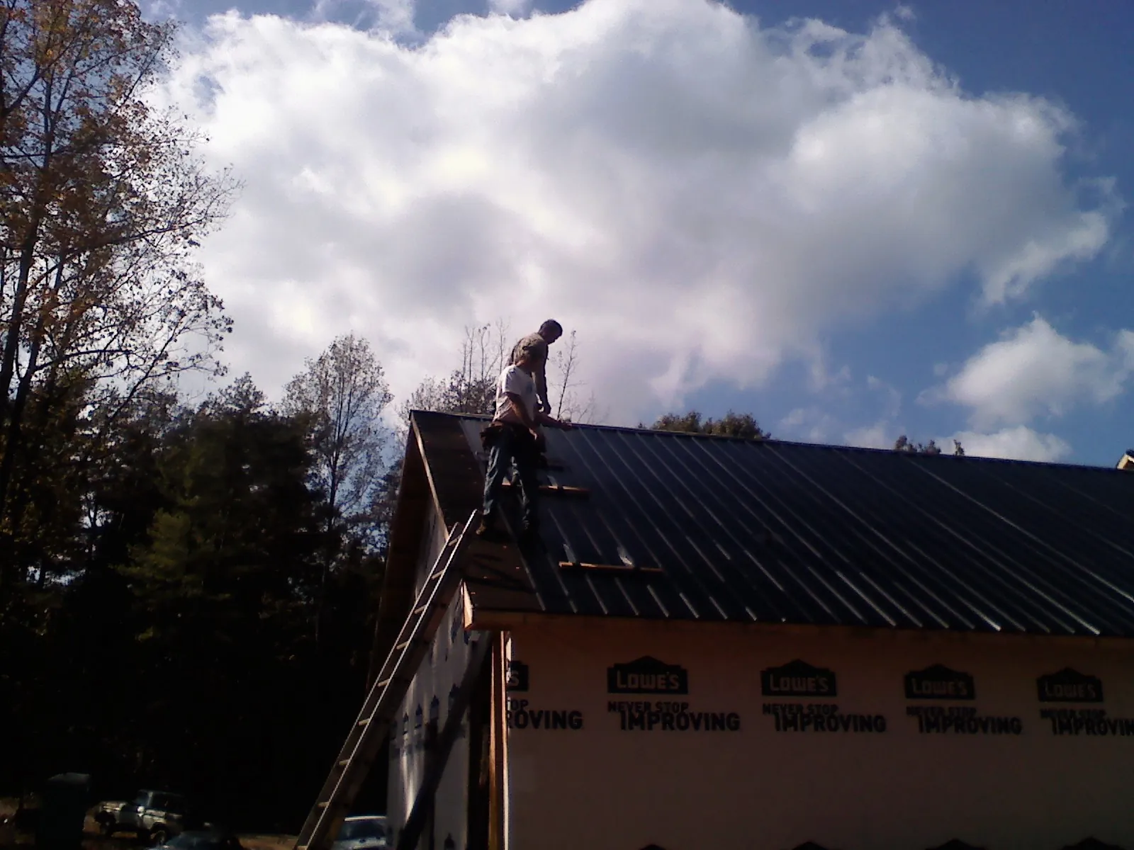 Roofer fastening dark metal panels high against a cloudy sky, from a Roof Inspection job in Cheswick