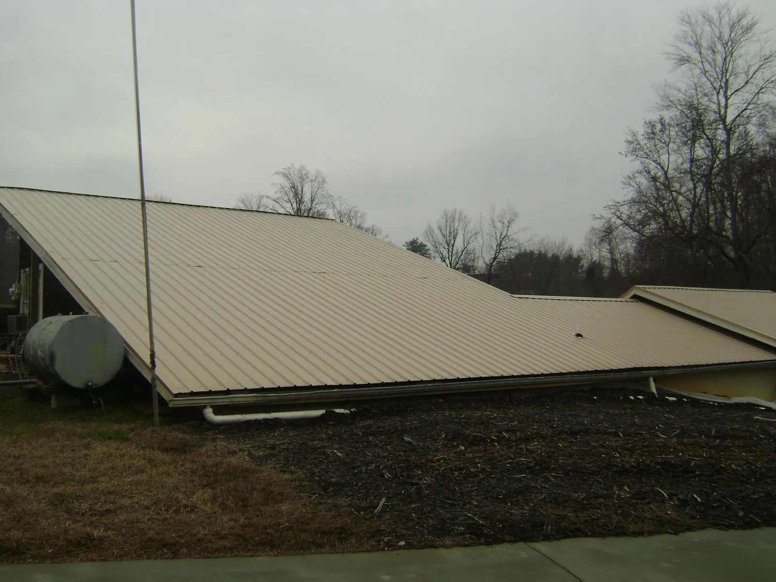 Wide tan metal roof plane seen from the ground beside a propane tank in Cheswick