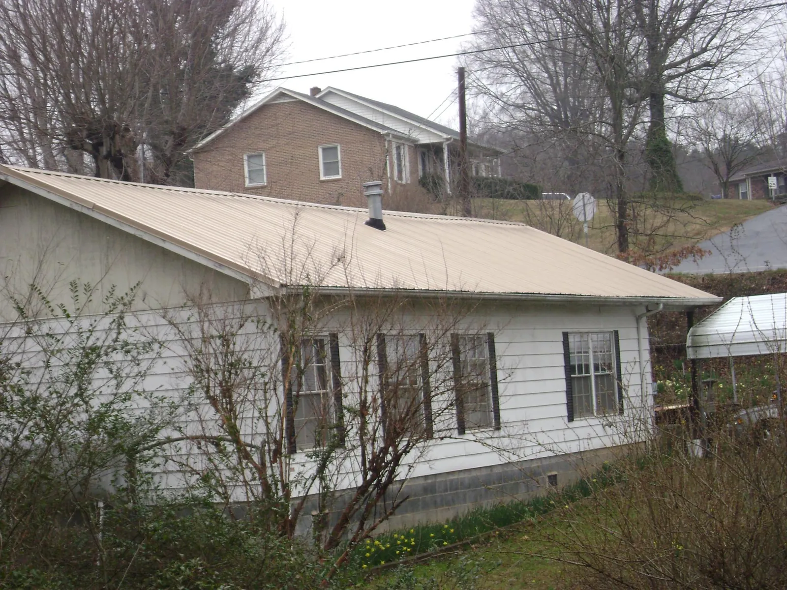 Tan metal roof on a white sided house set into a hillside — Commercial Roofing by Roofing Brothers in Cheswick